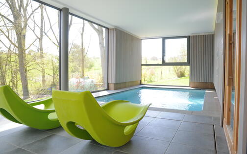 binnenzwembad met 2 groene ligstoelen ernaast, binnen in een villa