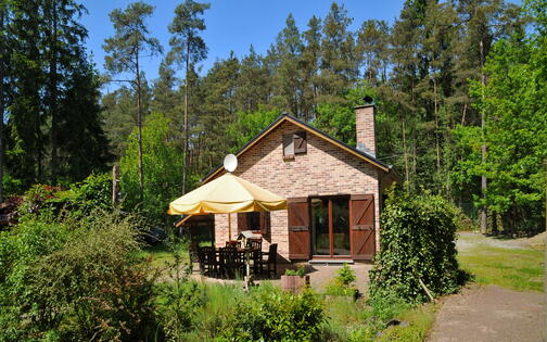 chalet in de groene bossen van de Ardennen, met terras waarop een tafel met 6 stoelen en gele parasol staan