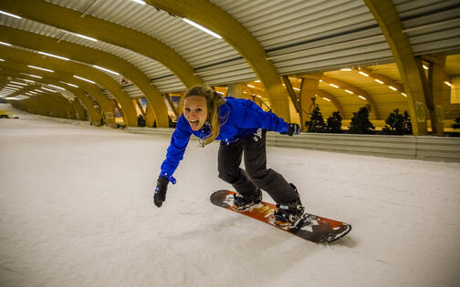 jonge vrouw met zwarte broek en blauwe jas snowboardt naar beneden