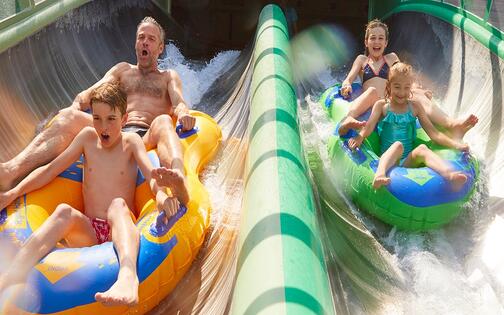dubbele waterglijbaan met rubber bootjes, links zit een vader met zoon en rechts 2 meisjes in een rubberbootje