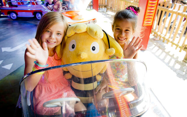 2 meisjes in een attractie in Plopsa Coo, in een botsauto met tussen hen een grote knuffel van Maya de Bij