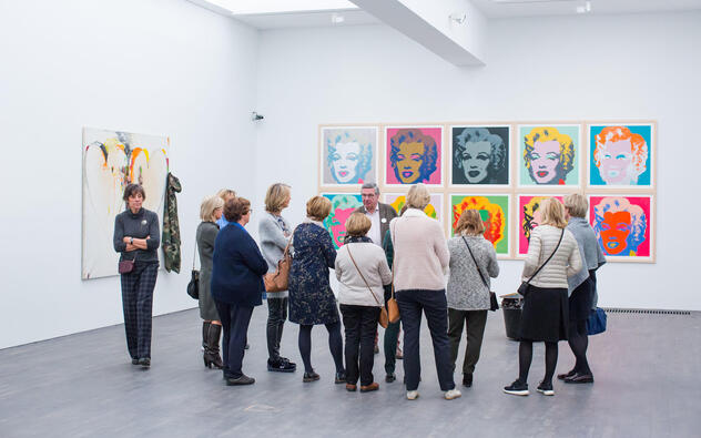 bezoekers kijken naar een aantal portretten van Marilyn Monroe door Andy Warhol