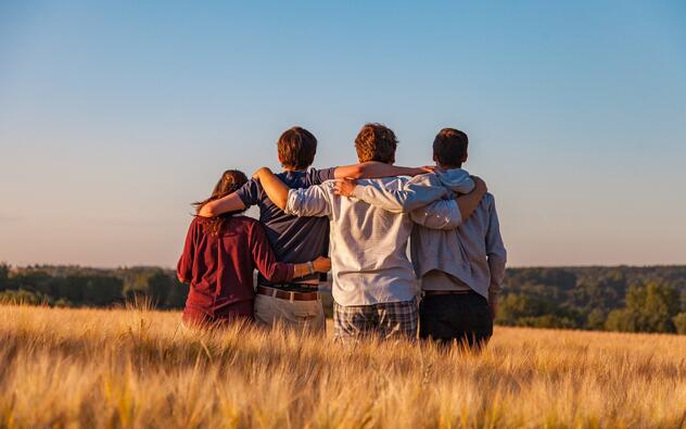 4 jongeren met armen om elkaar in een veld