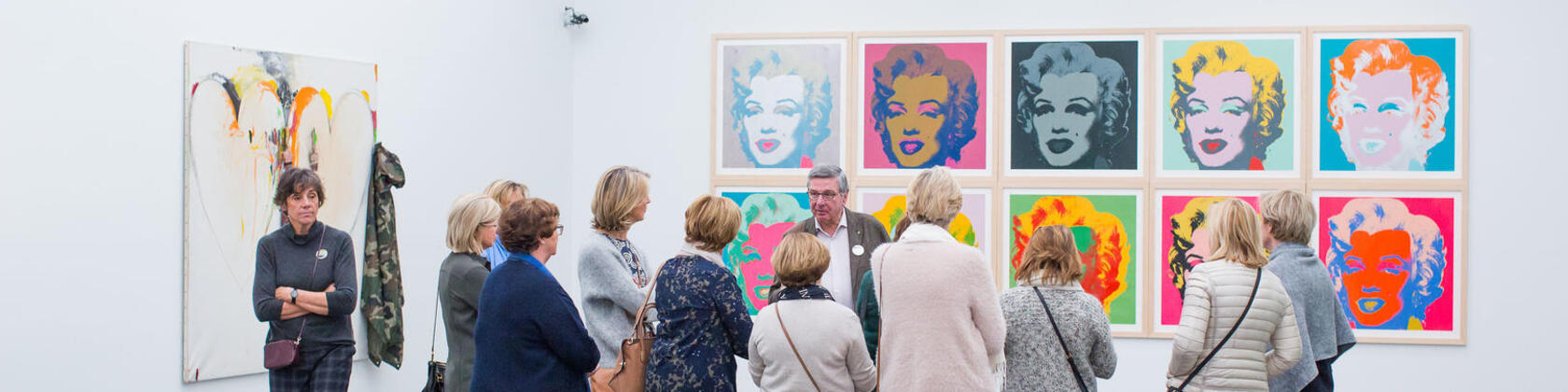 bezoekers kijken naar een aantal portretten van Marilyn Monroe door Andy Warhol